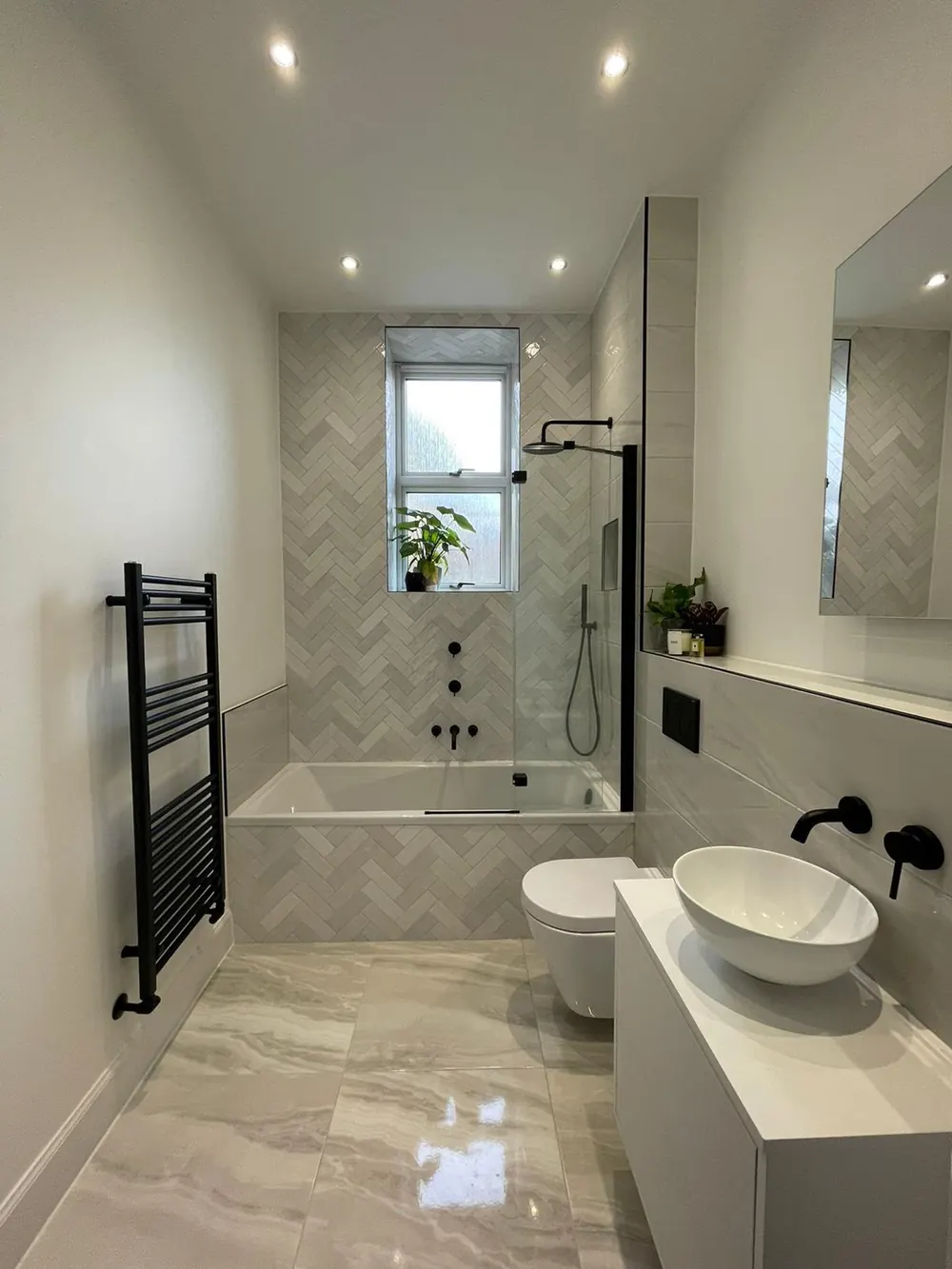 Herringbone-tiled bathroom with a bath, shower over, vessel basin and black towel radiator