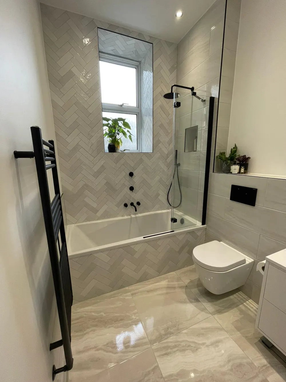 Wall-hung WC and bath with a shower over in a herringbone-tiled bathroom