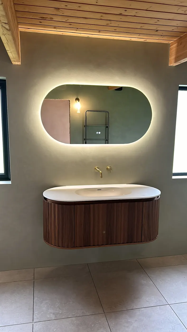 Ribbed walnut vanity unit with a backlit oval mirror and brass wall-mounted taps