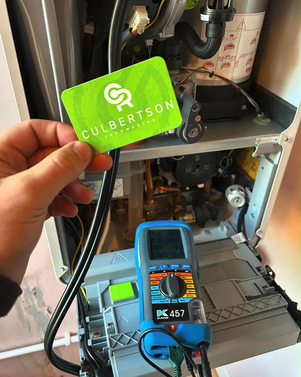 Culbertson Renewables card held in front of an open boiler with a flue gas analyser on test