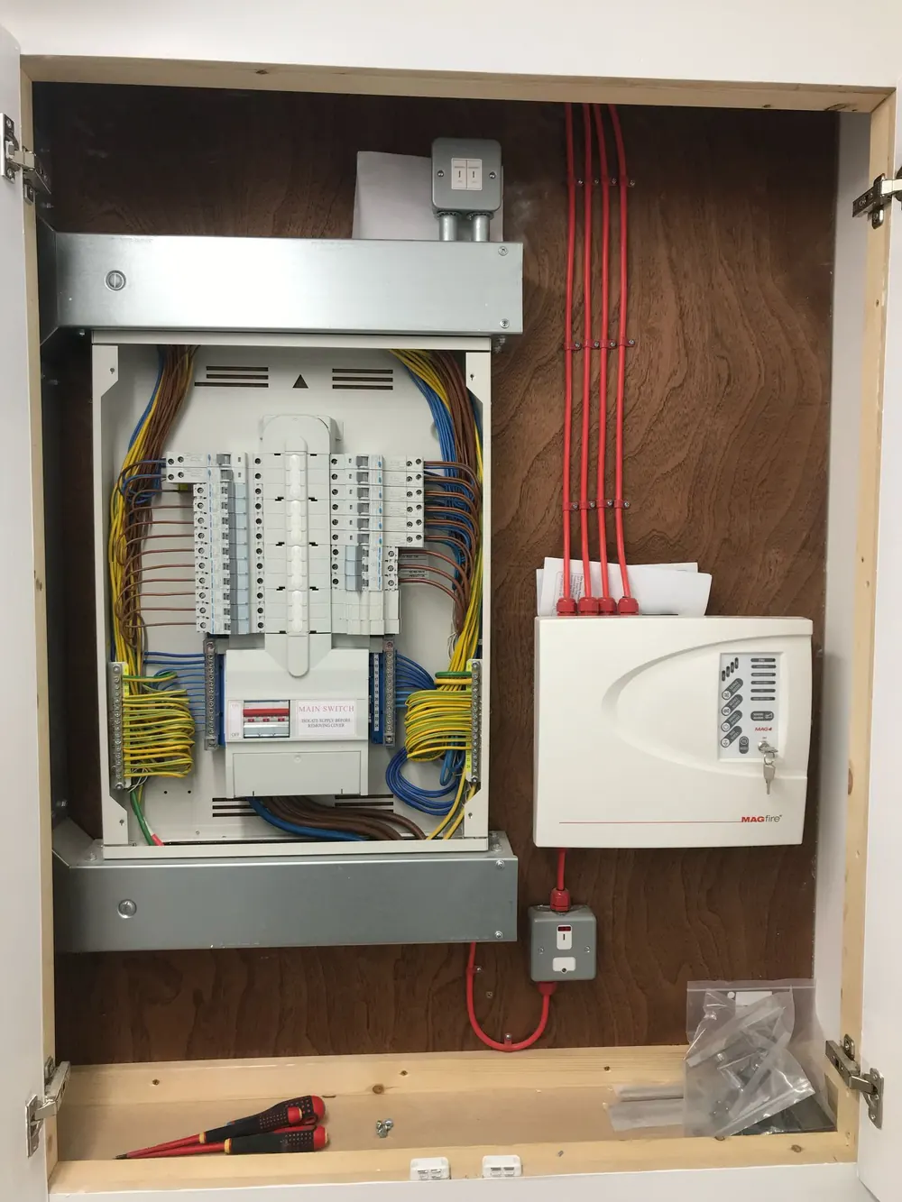 Three-phase distribution board wired out and labelled beside a fire alarm control panel