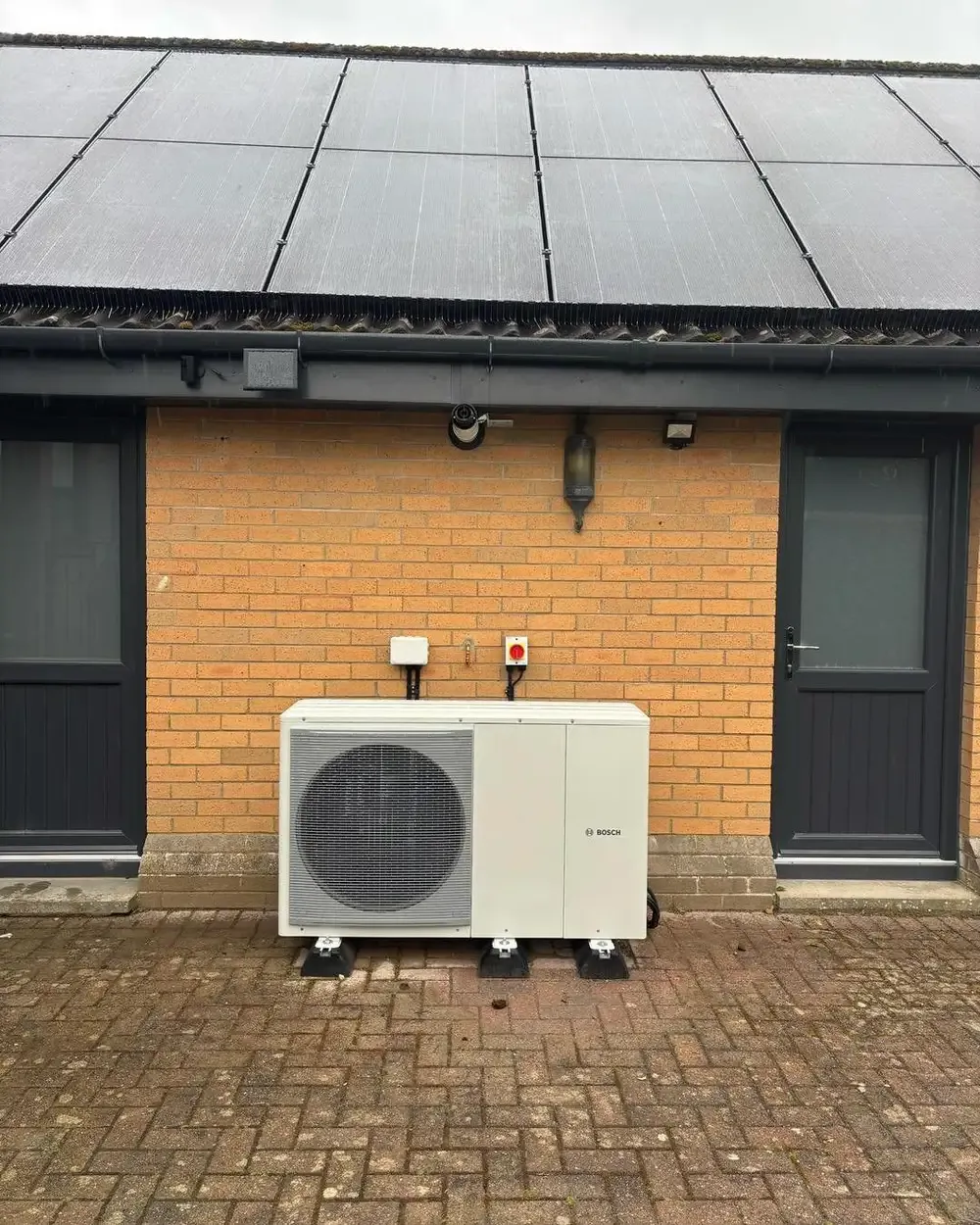 Bosch air source heat pump unit installed on a brick patio outside a home