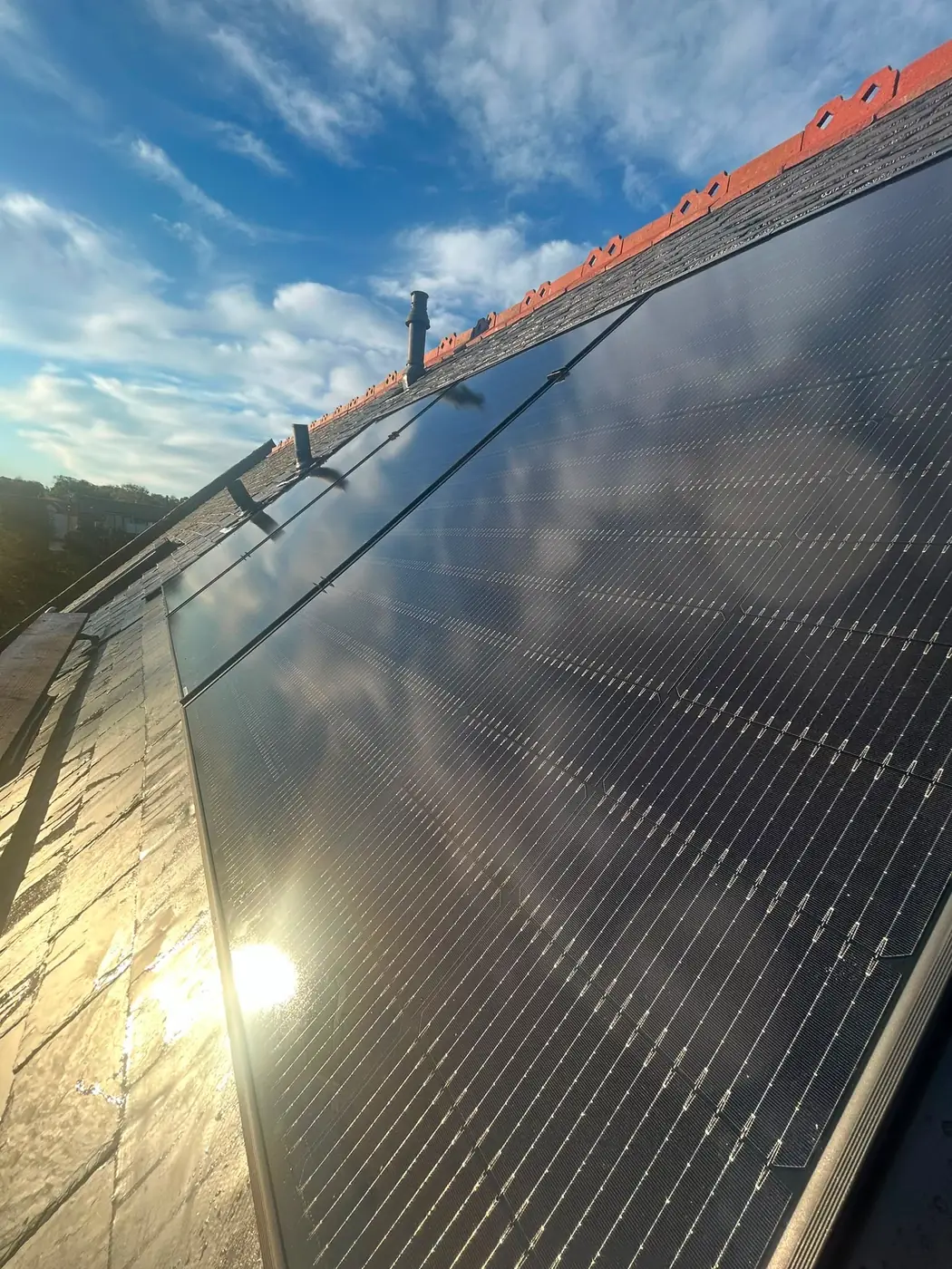 Solar PV panels installed across a slate roof, catching low sun