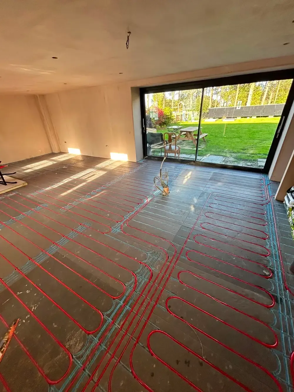 Underfloor heating loops laid across a room opening onto a garden through full-height glazing